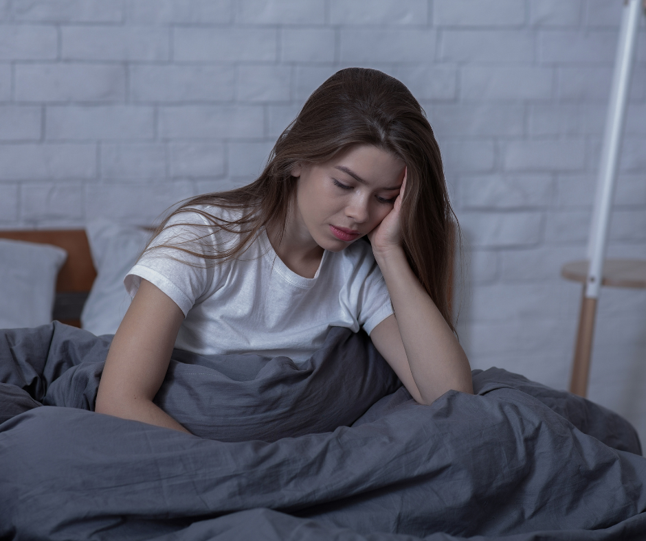 Person lying in bed looking fatigued, experiencing symptoms of Seasonal Affective Disorder (SAD) during winter.